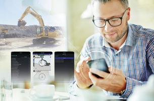 Man using Smart Construction Remote on phone with excavator in the background